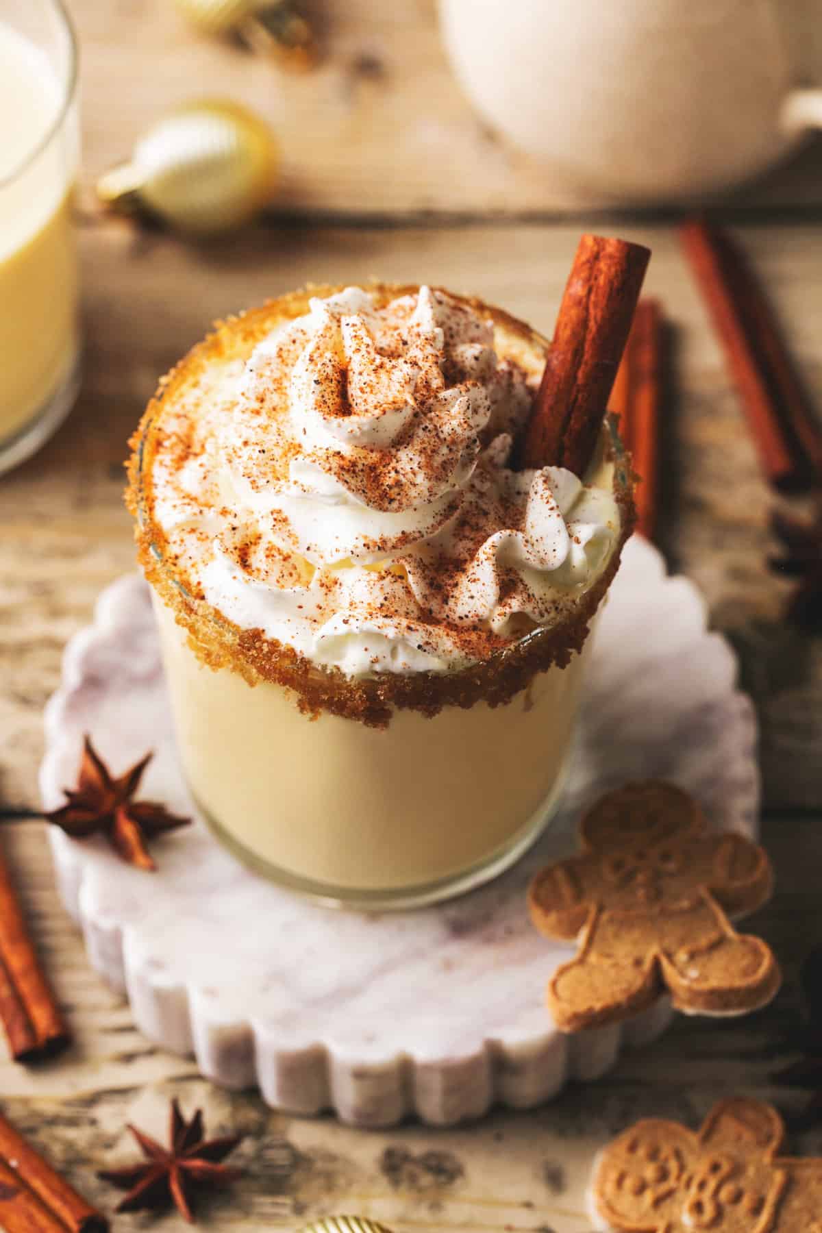 glass of eggnog with chipped cream with cinnamon stick on coaster