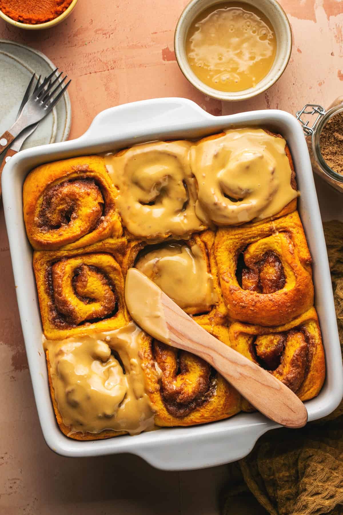 partially frosted pumpkin cinnamon rolls in pan with wooden knife and maple icing