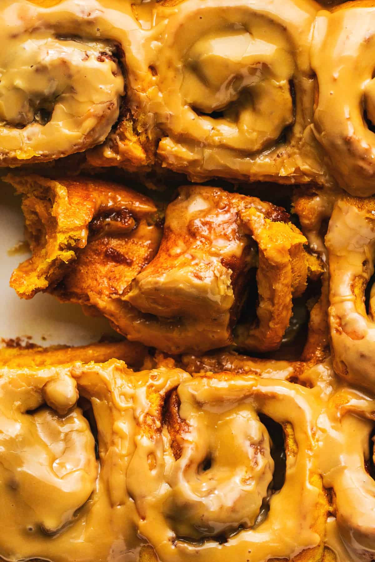 up close view of cinnamon rolls in pan with one. partly unrolled showing filling