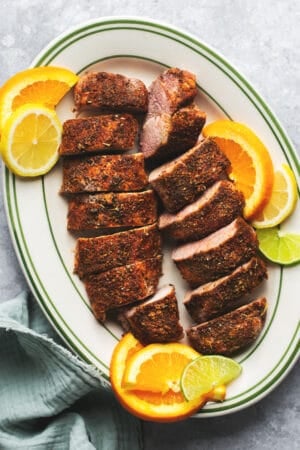 sliced pork tenderloin on platter with slices of lime and oranges