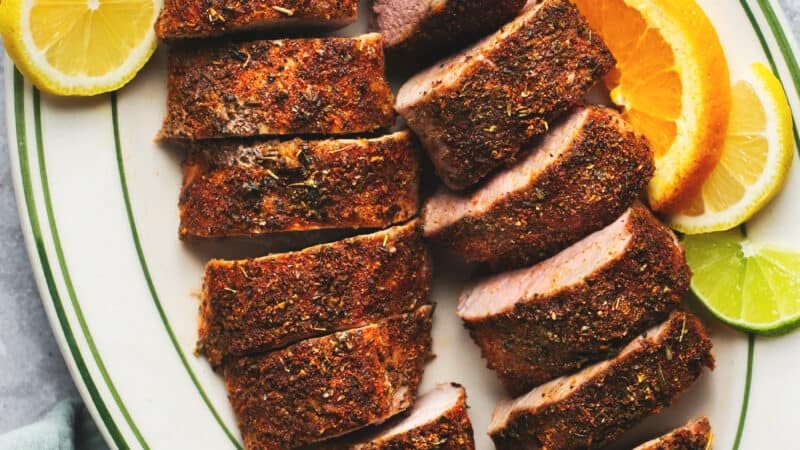 sliced pork tenderloin on platter with slices of lime and oranges