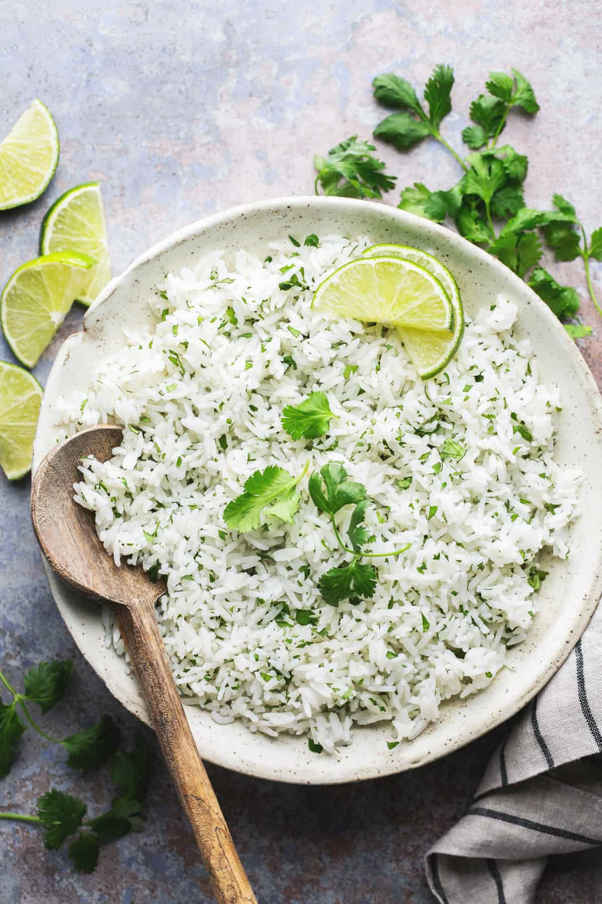 serving bowl of cooked white rice with cilantro garnish and lime wedges
