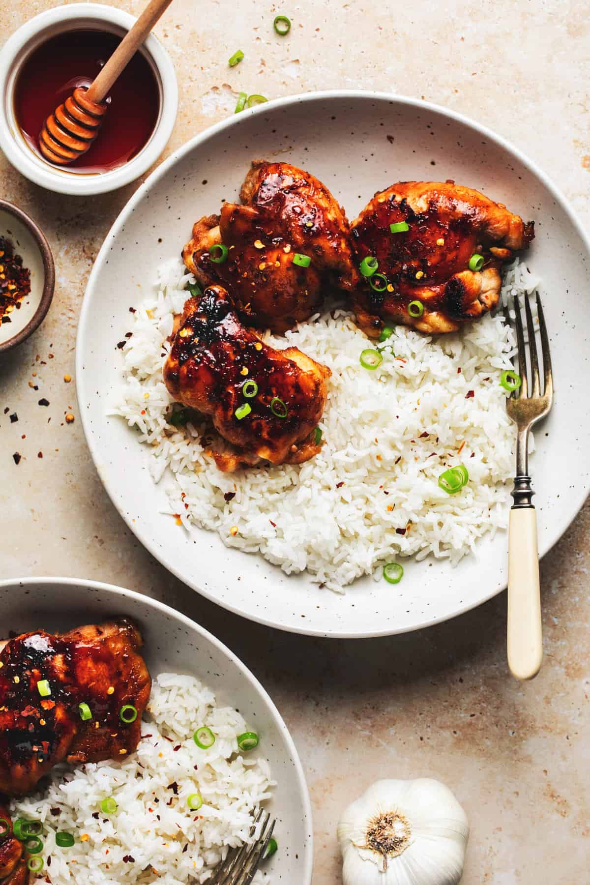 two plates of chicken thighs with rice and honey glaze in side dish