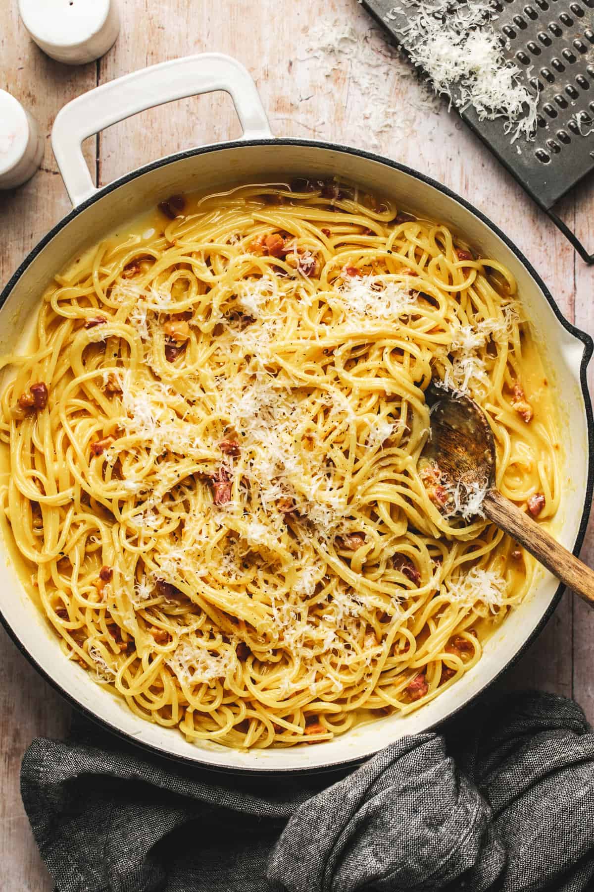 spaghetti noodles in a skillet with parmesan and wooden spoon