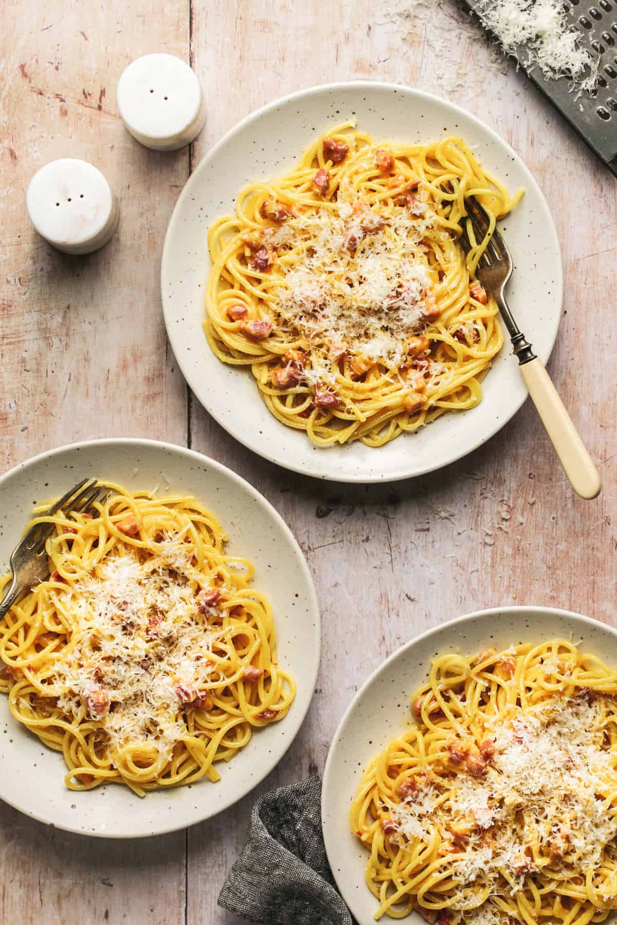 three bowls of spaghetti noodles with pancetta and parmesan cheese and forks