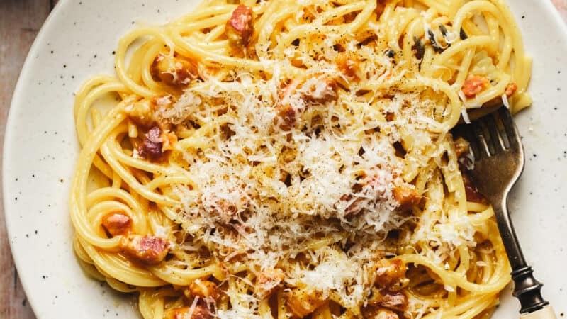 one plate of spaghetti carbonara noodles with pancetta and parmesan cheese with fork in dish