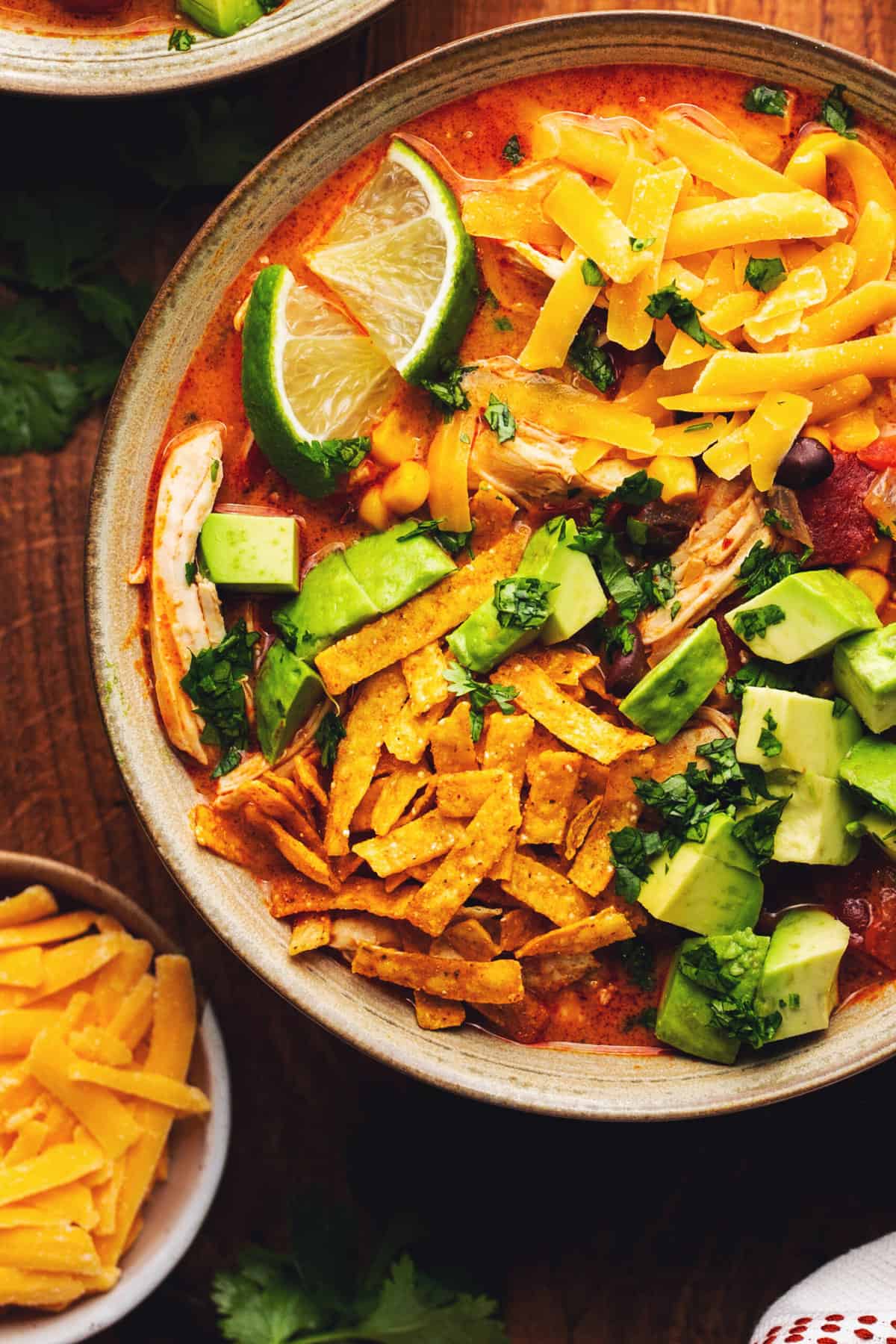 bowl of soup topped with avocado, tortilla strips, lime wedges, and cilantro