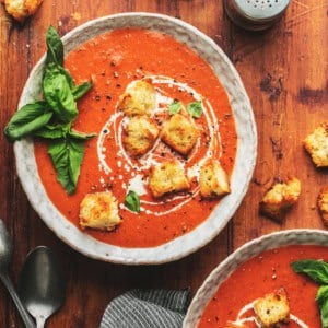two bowls of creamy tomato soup topped with basil and croutons