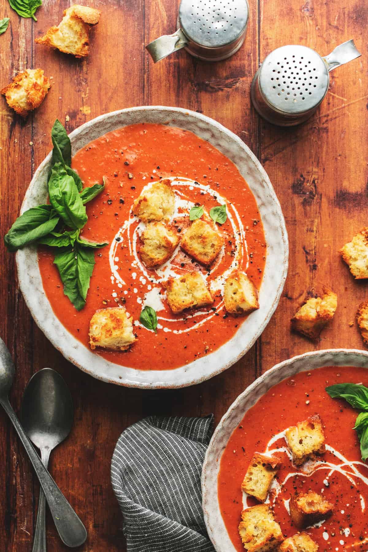 two bowls of creamy tomato soup topped with basil and croutons