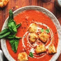 overhead view of bowl of tomato soup with croutons and fresh basil