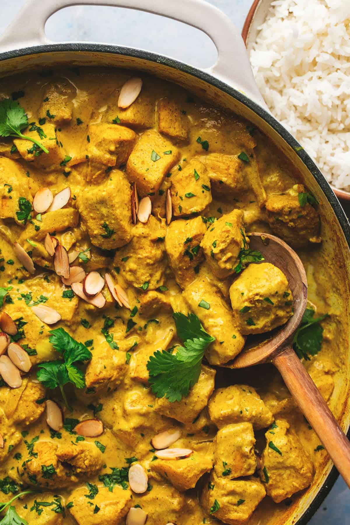 half of a skillet with mango chicken curry and wooden serving spoon