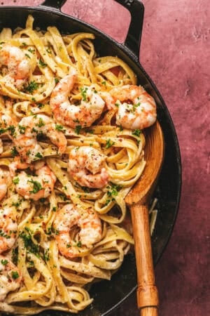 shrimp alfredo pasta in a skillet with wooden serving spoon
