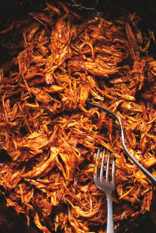 two forks shredding chicken in bbq sauce