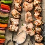 spooning bang bang sauce onto chicken skewers