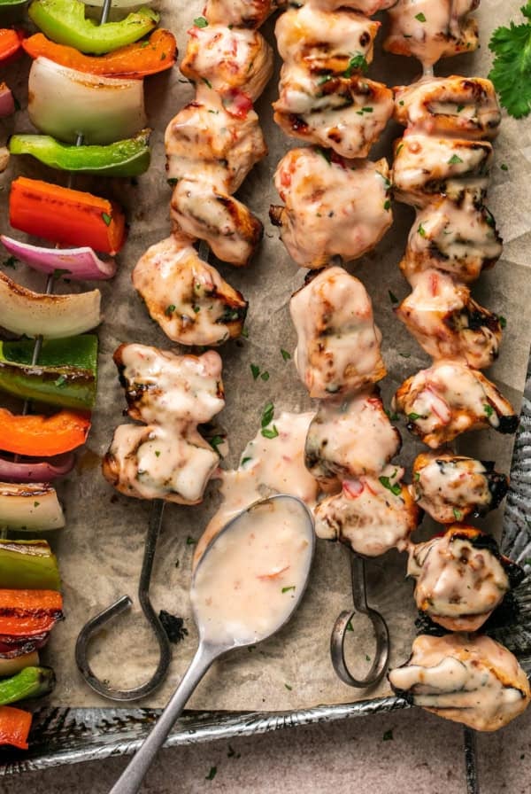 spooning bang bang sauce onto chicken skewers