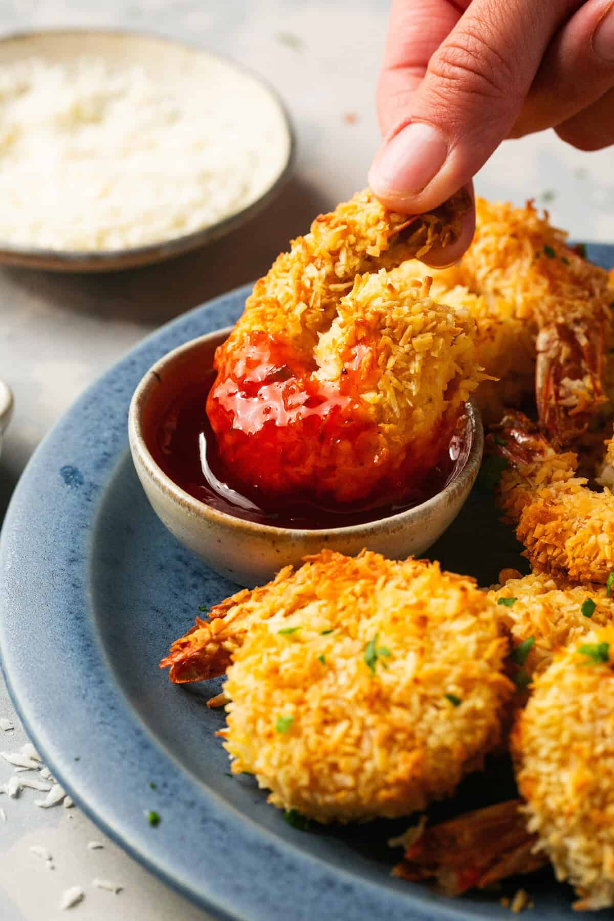 hand dipping coconut shrimp into sweet and sour sauce.