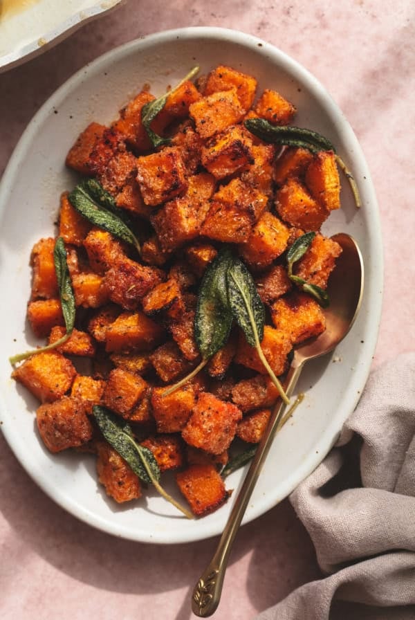 cubed and roasted butternut squash on serving dish with spoon and napkin