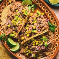 overhead view of three shredded pork tacos on a platter with lime wedges