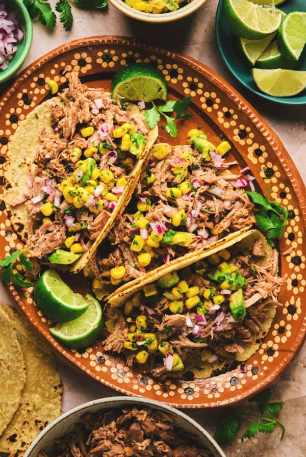 overhead view of three shredded pork tacos on a platter with lime wedges