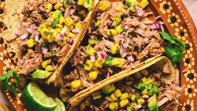overhead view of three shredded pork tacos on a platter with lime wedges