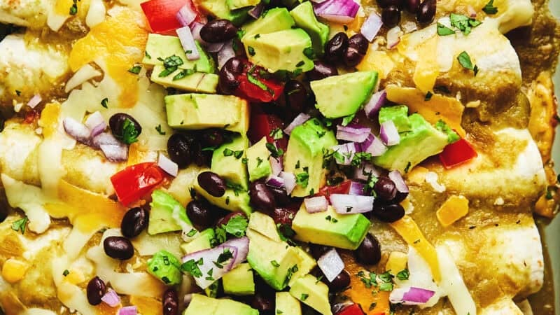 up close avocado, black beans, and tomatoes on top of enchiladas