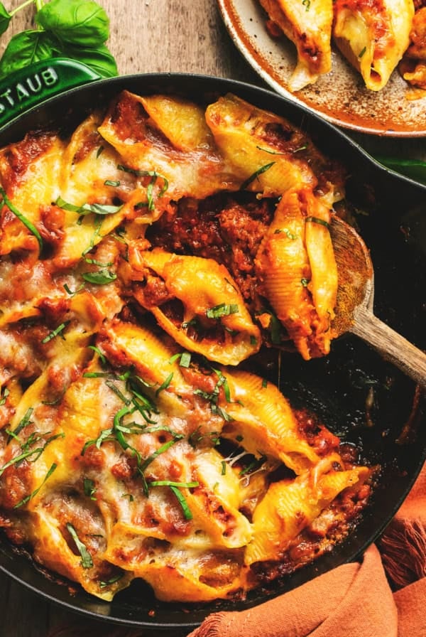 sausage stuffed pasta shells with fresh basil and meat sauce in skillet with spoon
