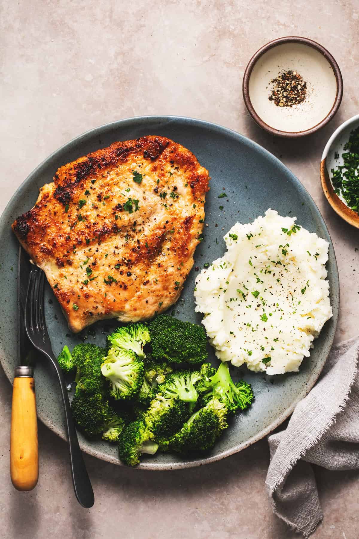 cooked chicken breast on plate with fork, mashed potatoes, and broccoli
