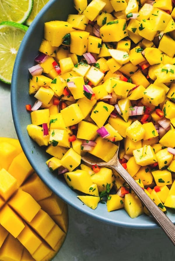 spoon dipping into bowl of diced mangoes with onions and cilantro