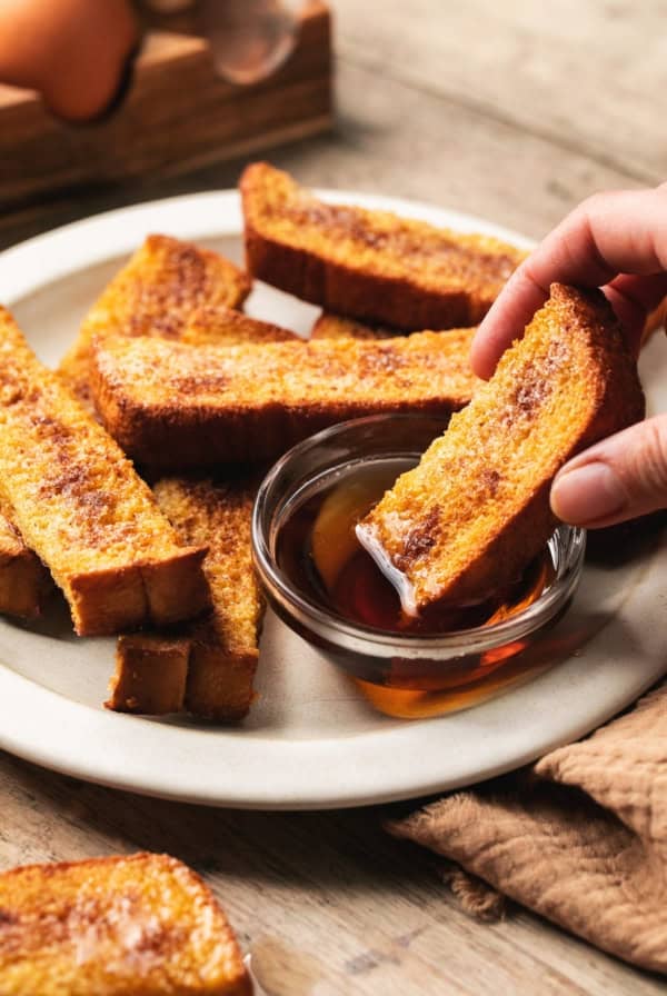 hand dipping french toast into syrup bowl