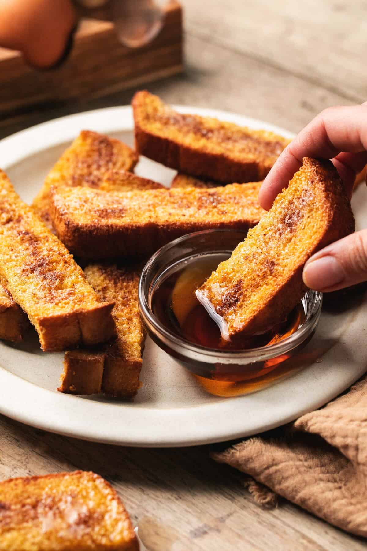 hand dipping french toast into syrup bowl.