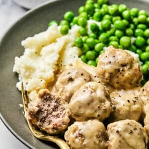 Close up of Swedish meatballs on a grey plate, with one cut open, sitting on a fork.