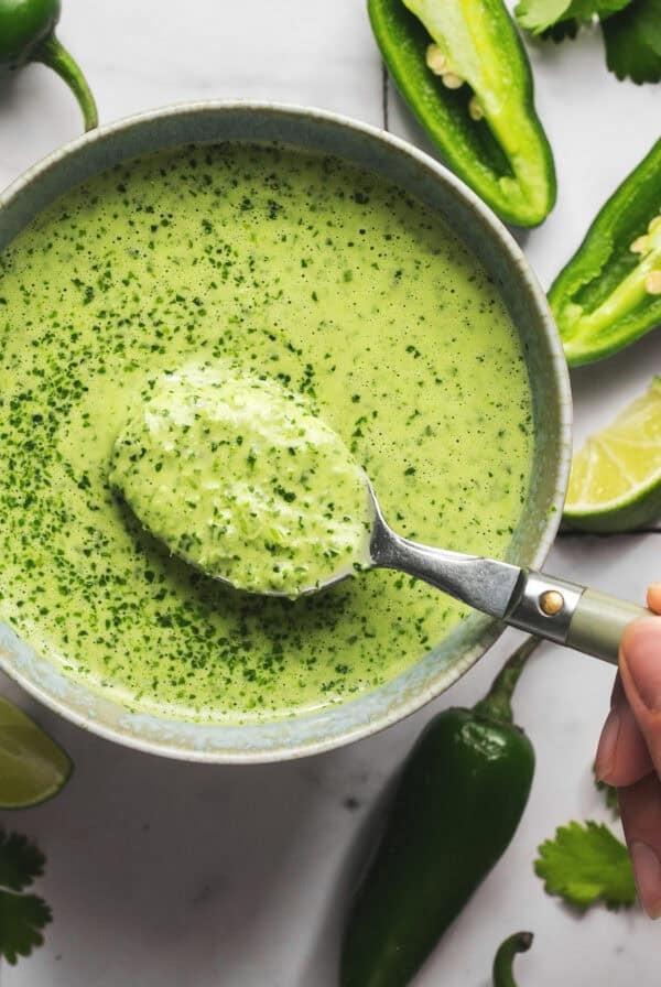 spoon scooping green herby jalapeno sauce from bowl.