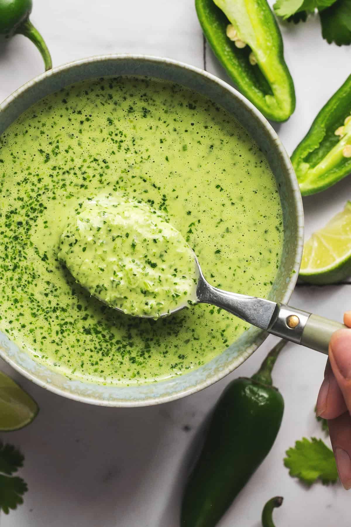 spoon scooping green herby jalapeno sauce from bowl. 