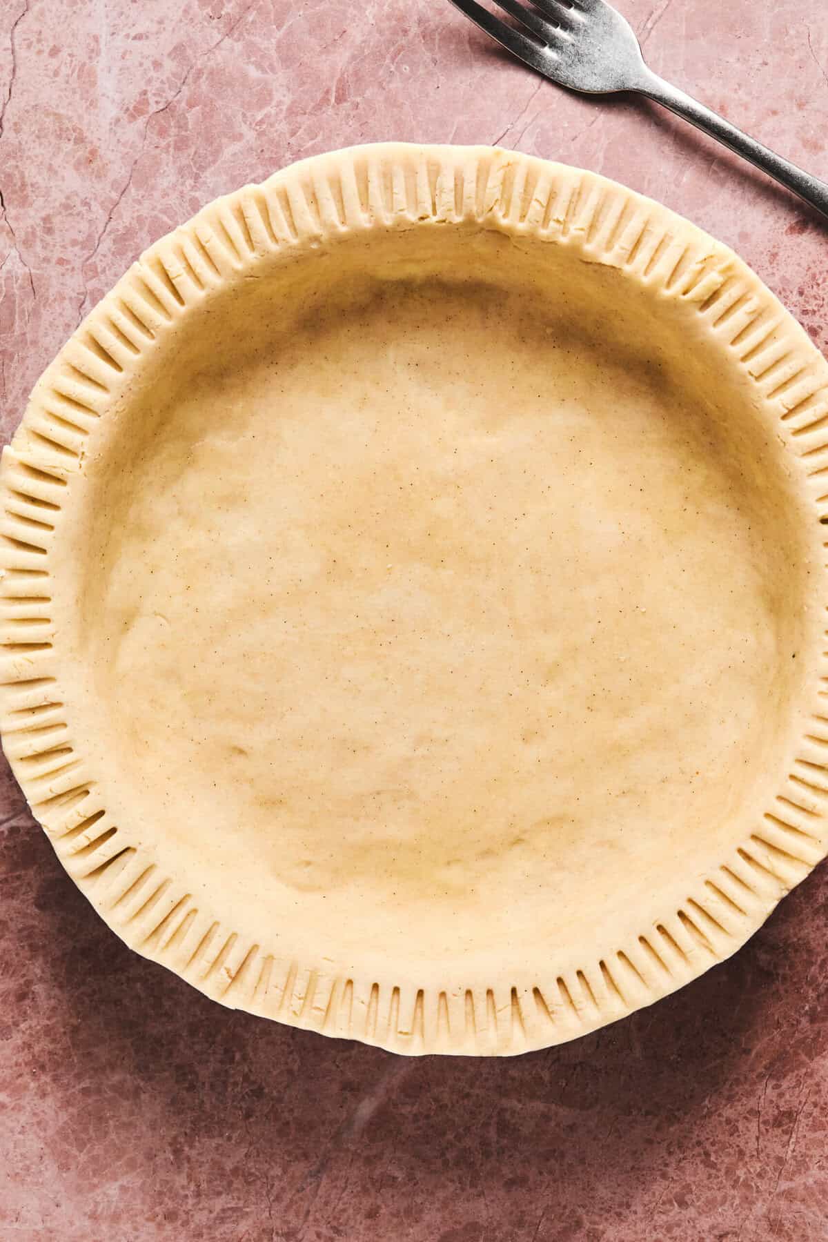 Unbaked gluten free pie crust on table with fork.