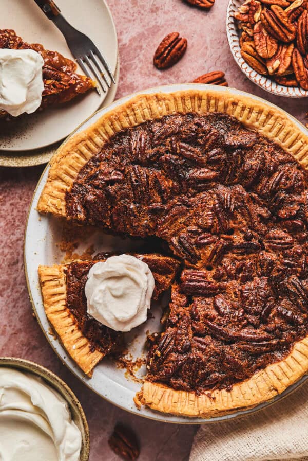Over head of pecan pie with a piece cut and whipped cream on top all in a pie tin.