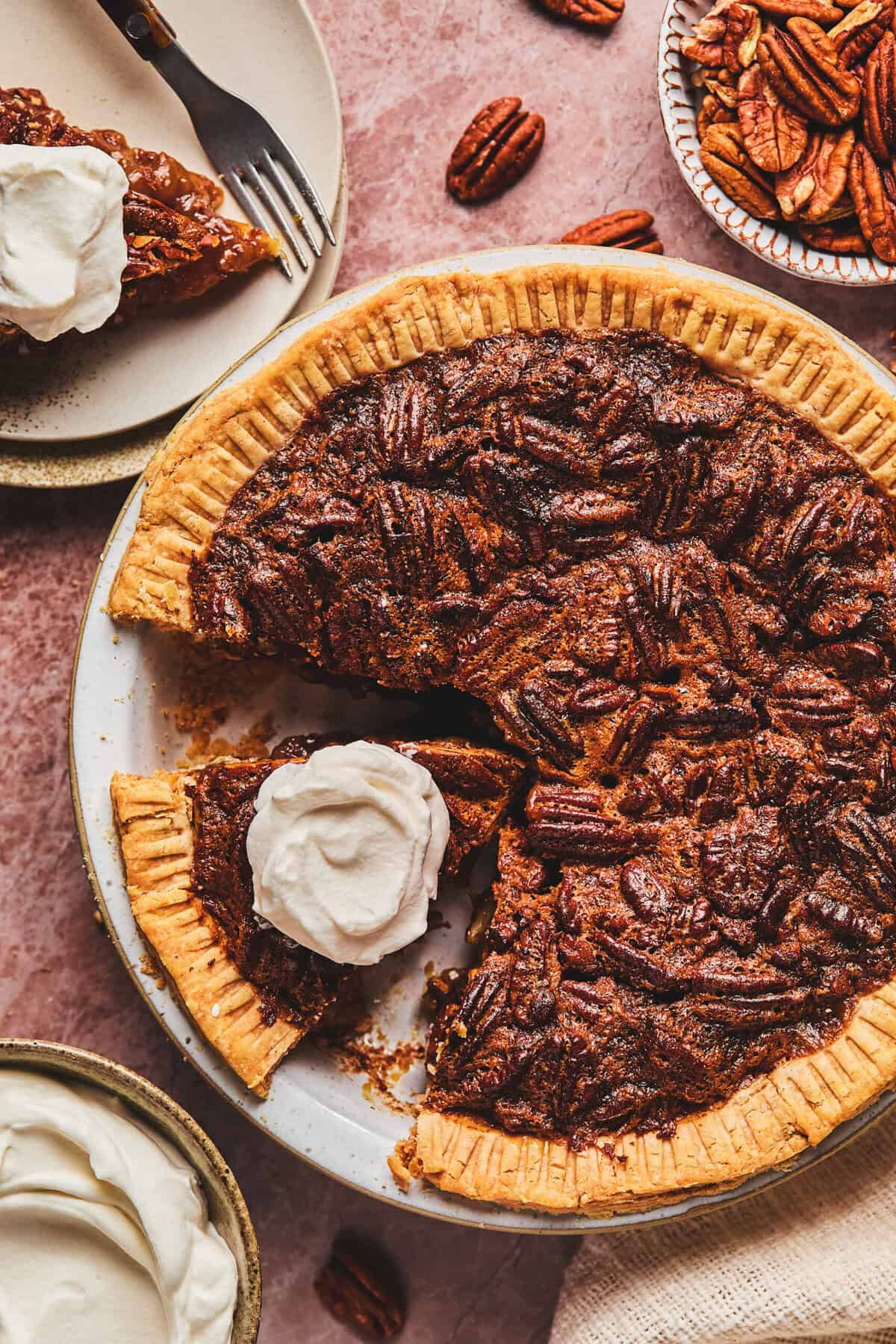 Over head of pecan pie with a piece cut and whipped cream on top all in a pie tin.