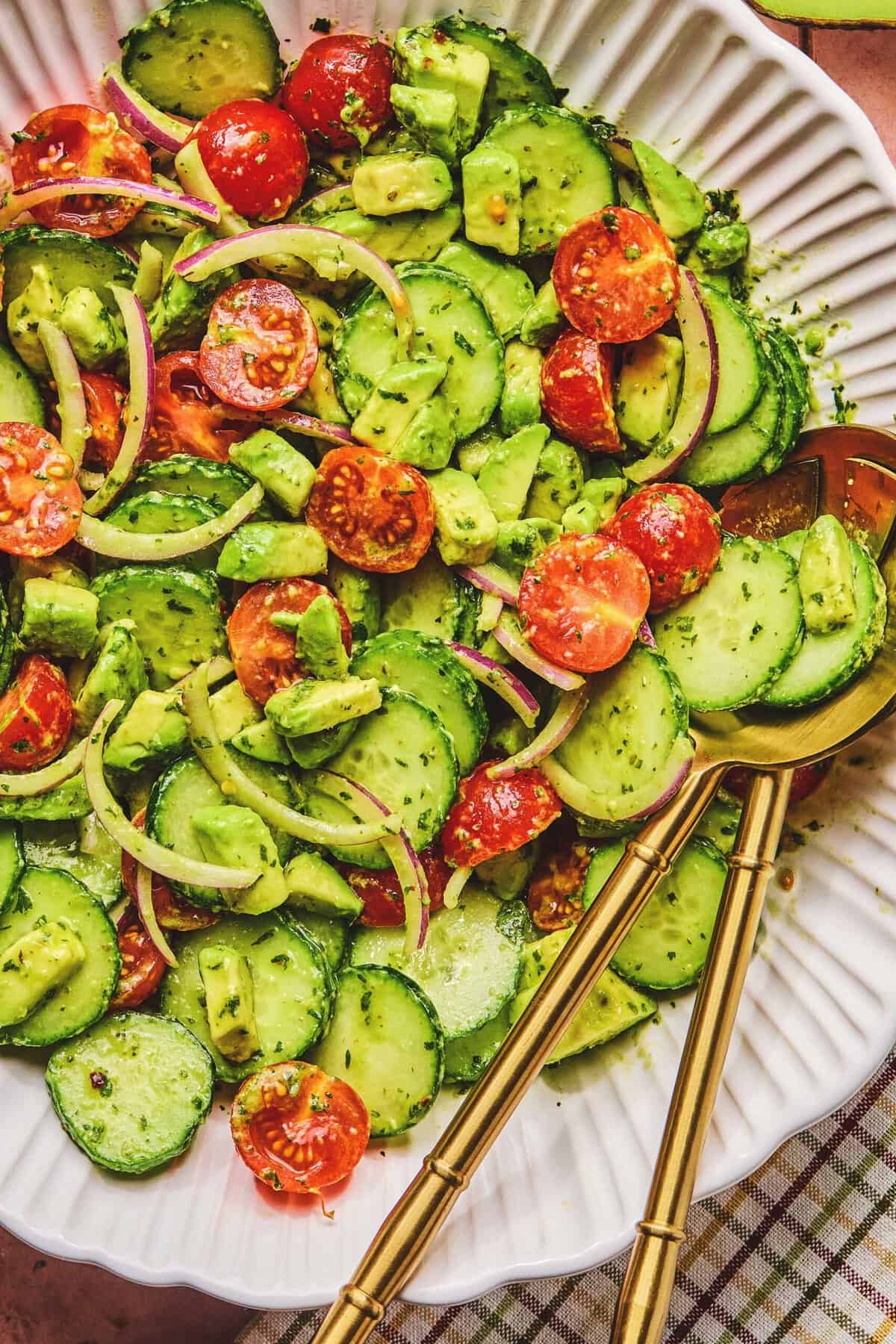 Overhead close up of avocado salad and serving utensils in a serving bowl.