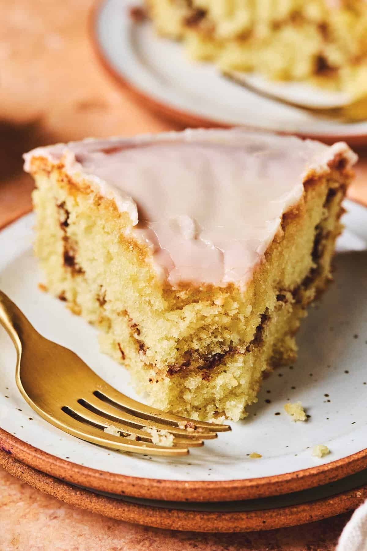 Close up of a piece of honey bun cake with a bite missing on a plate with a fork.