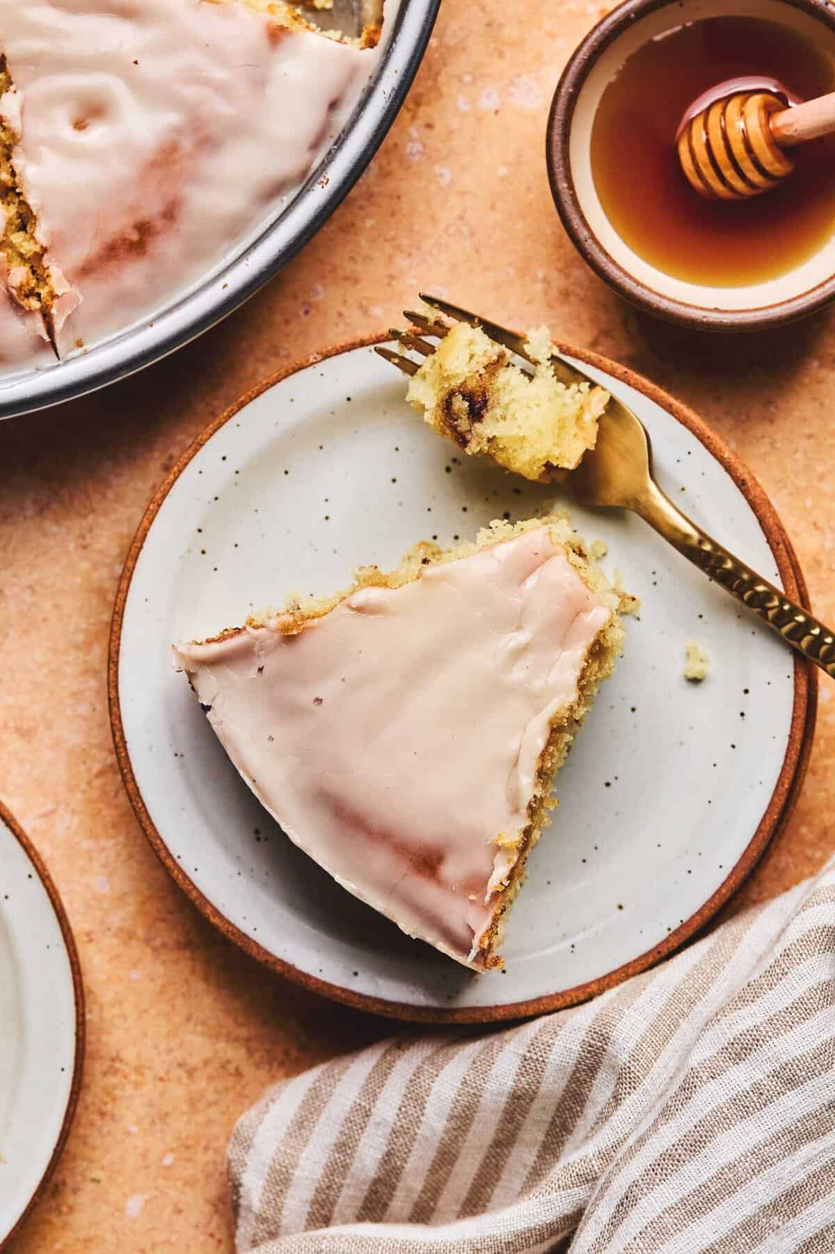 Overhead of a piece of honey bun cake with a piece missing and a fork with the bite on top all on a plate.