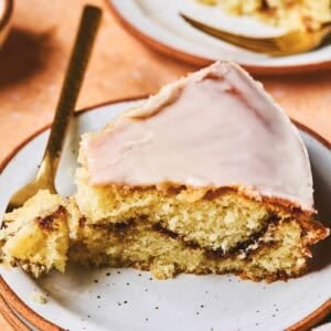 A piece of honey bun cake with a fork with a bite on it all on a plate.