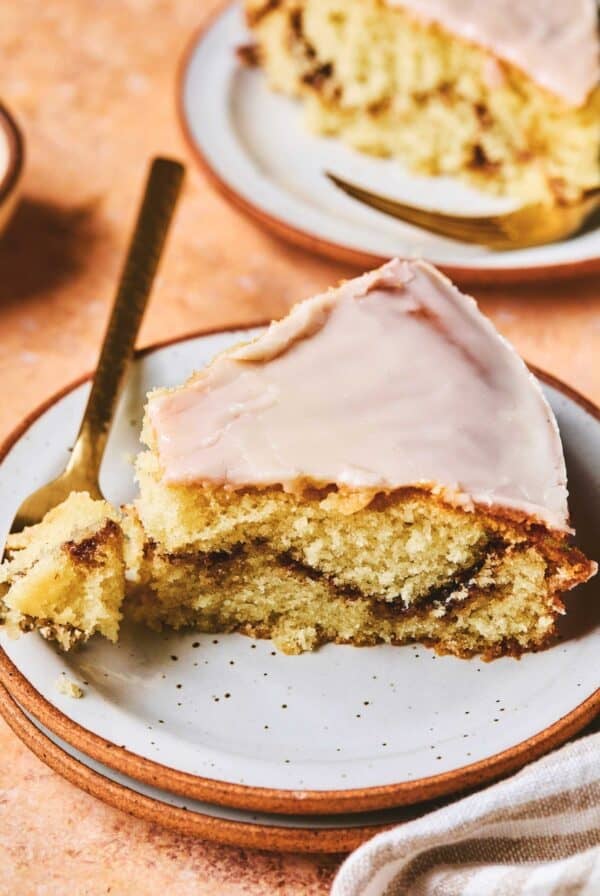 A piece of honey bun cake with a fork with a bite on it all on a plate.