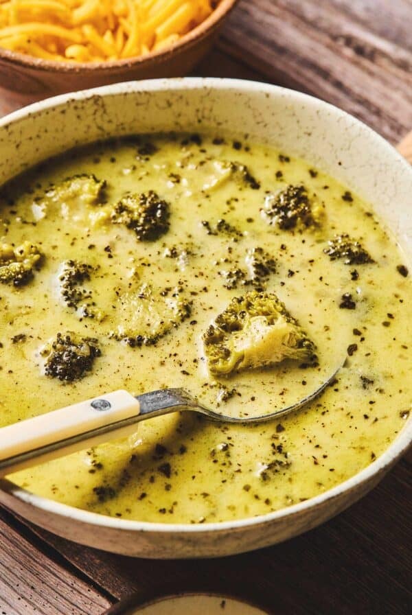 Close up of slow cooker broccoli cheddar soup with a spoon in a bowl.