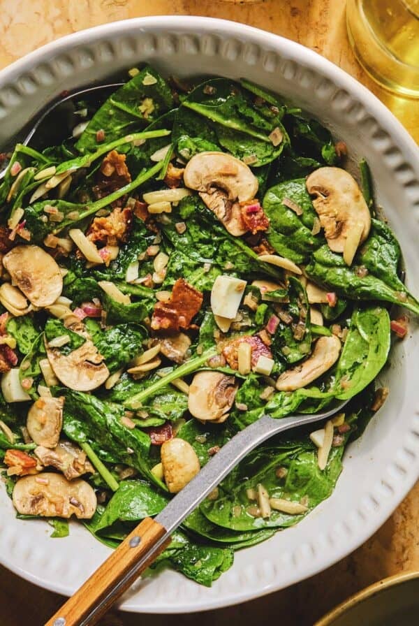 Overhead of spinach salad with hot bacon dressing with a serving spoon in a dish.
