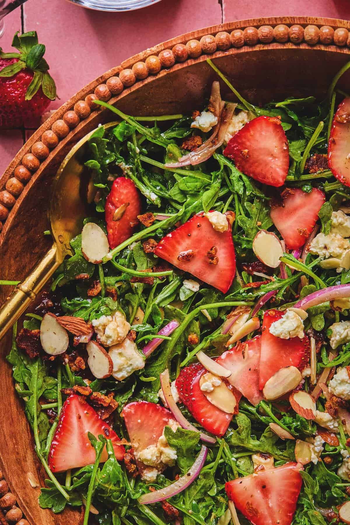 Close up overhead of strawberry arugula salad and a serving spoon in a serving bowl.