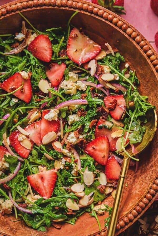 Overhead of strawberry arugula salad with a serving spoon in a serving dish.