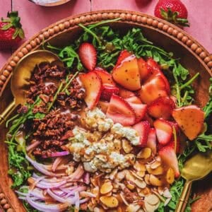 Overhead of unmixed strawberry arugula salad with a serving spoon in a serving bowl.